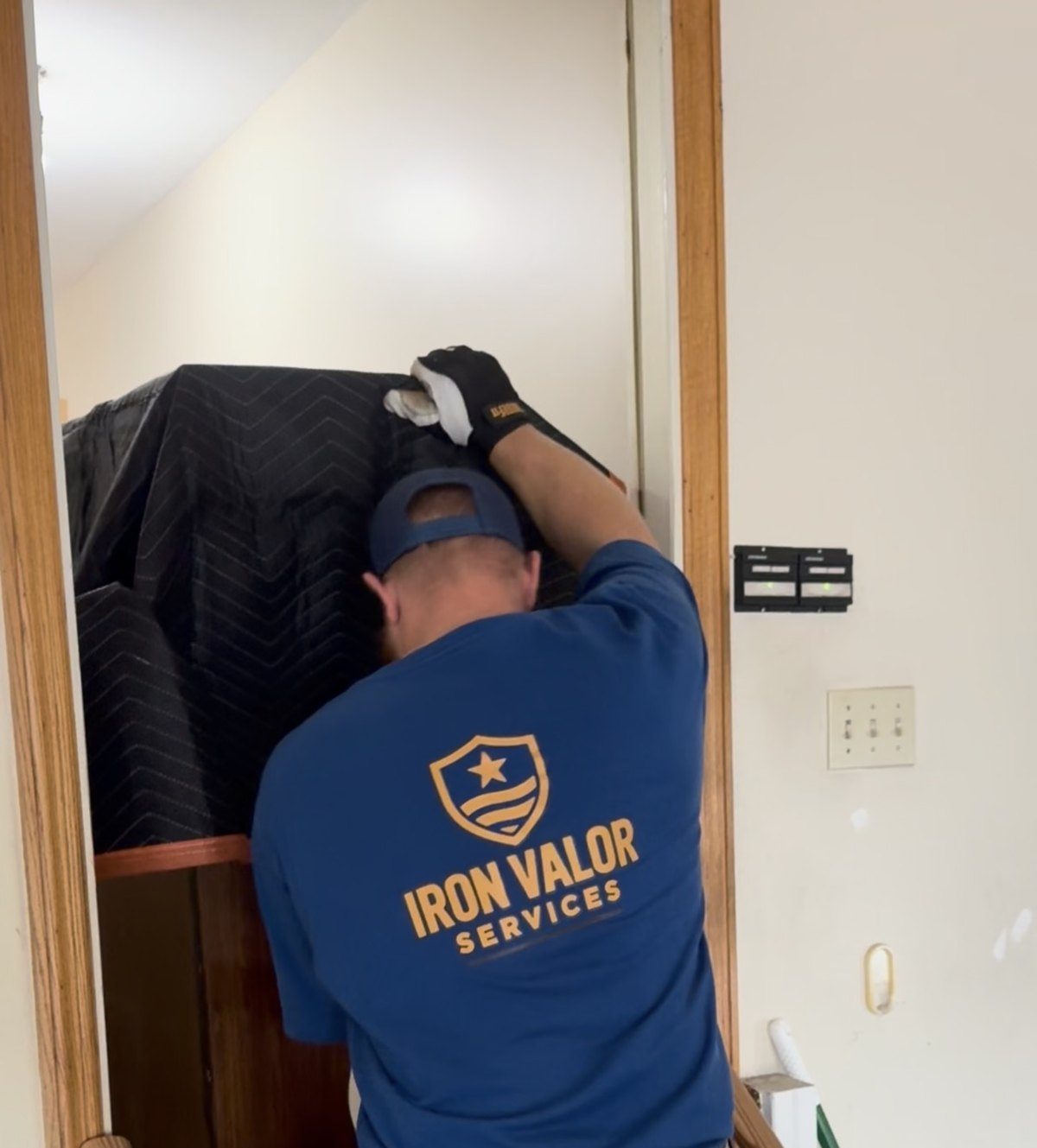 An Iron Valor crew member carrying a blanket-wrapped cabinet down a narrow staircase.